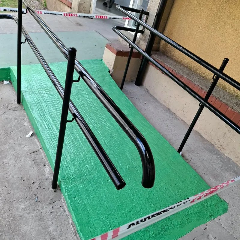 Barandas de caño negras a los dos lados de una rampa de acceso pintada de verde
